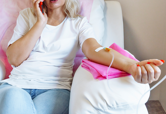 Woman sitting on a chair after donating blood, talking on a red phone while a needle and tubing are in her left arm.