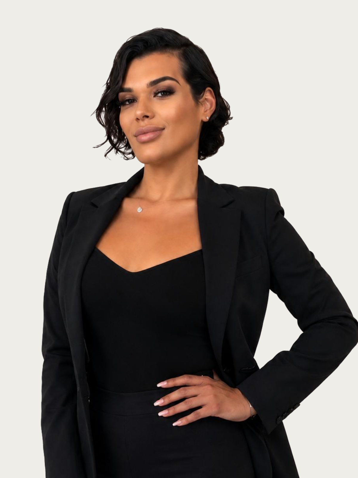 Professional woman in a black blazer and matching top, posing with one hand on her hip against a light background.